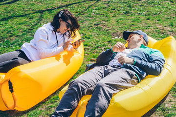 couple laying on inflatable mattress in city park at sunny day. talking and chatting
