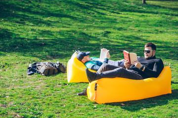 two men friends laying on yellow inflatable mattress reading books