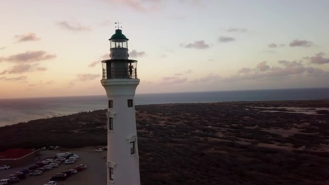 A man takes photos of Aruba from the top of the California Lighthouse during a beautiful orange sunset. Aerial sweep.