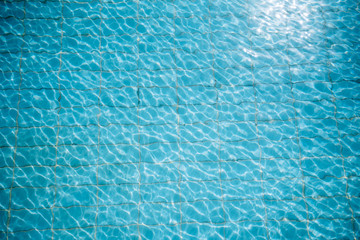 Water ripples on blue tiled swimming pool background. View from above.