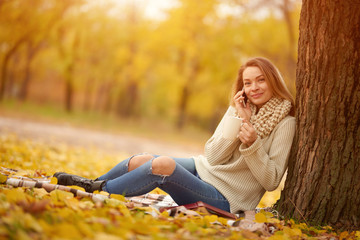 Beautiful girl talking on the phone in a warm autumn park. Concept of autumn warmth, atmosphere and comfort. With space for an inscription