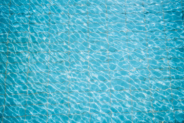 Fototapeta na wymiar Water ripples on blue tiled swimming pool background. View from above.