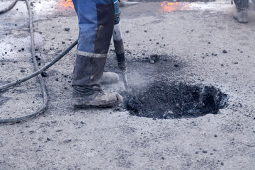 Closeup of a photo of professional workers in uniform repairing asphalt road with a jackhammer. Concept renovation, major repairs of the main street in the city, road construction, pits