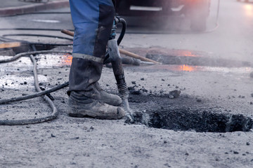 Closeup of a photo of professional workers in uniform repairing asphalt road with a jackhammer....