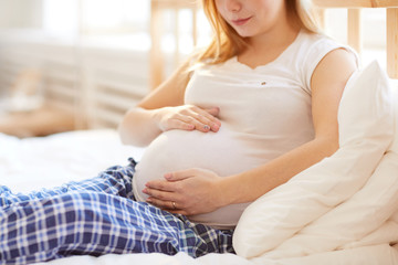 Mid section portrait of pregnant woman hugging big belly lying on comfortable bed at home, copy space