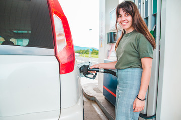 young pretty woman at gas station filling up car tank
