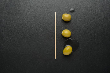 Fototapeta na wymiar Aceitunas verdes y palillos en la tabla de piedra negra