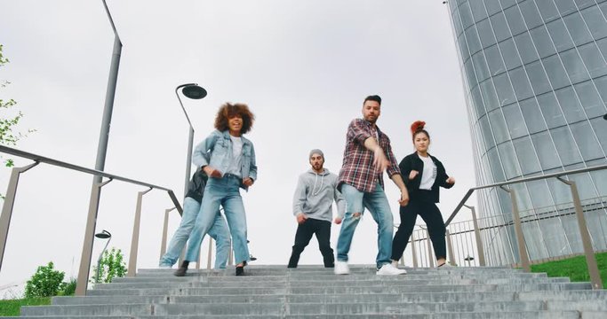 Slow motion of group of young urban dancers of different ethnicities are having fun to training in a city center with skyscrapers.