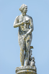 Ancient statue covered with moss and lichen of a sensual renaissance era woman in Potsdam, Germany