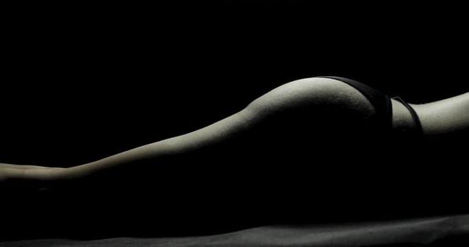 Close-up pan across a dimly lit sexy female body from feet to bum