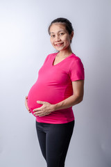 Side view midsection of a pregnant woman with hands holding tummy on white background