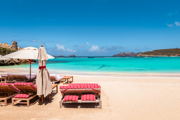 Beach chairs and umbrella on tropical beach. Summer vacation and relaxation background.
