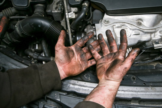 A picture of dirty hands of a guy from the garage above the enigne of a car. Hard and dirty work is behind him. 
