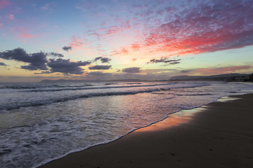 Location place Agia Marina Beach, island Crete, Greece. Sea coast spangled by rocks, the sunrise is reflecting on the wet sand. Morning landscape with mountains. Romantic relax place.