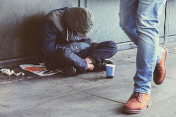 Homeless adult man sitting on the street in the shadow of the building and begging for help and...