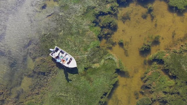 Aerial drone view of fly fisherman fishing from boat in lake over colorful weeds