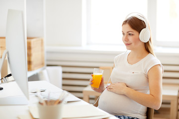 Obraz na płótnie Canvas Portrait of pregnant woman drinking orange juice watching health videos at home, copy space, copy space