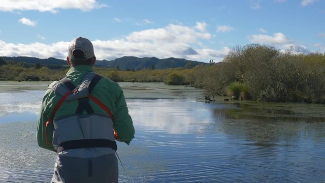 Fly fisherman stripping in line to catch a fish from a boat in a lake