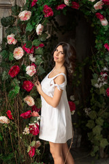 Beautiful brunette woman in white dress standing near the bushes with roses