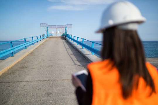 Ingegnere donna giovanissima di spalle su un pontile industriale sull'Oceano.