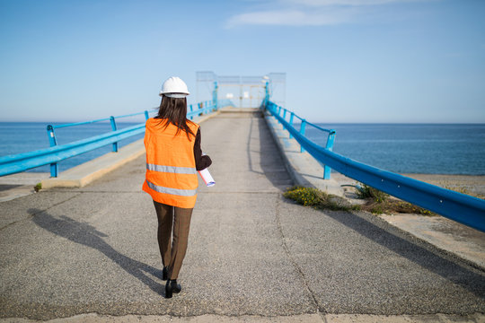 Ingegnere donna giovanissima di spalle su un pontile industriale sull'Oceano.