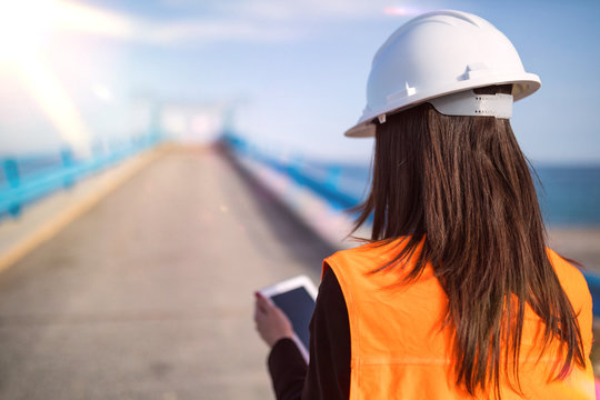 Giovane ingegnere donna con caschetto bianco che guarda verso il mare su un ponte da costruire