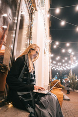 side view of young woman using laptop on street with night city