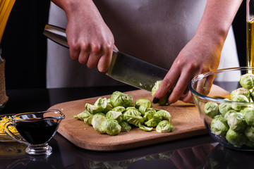 young woman cuts Brussels sprouts on a wooden cutting board