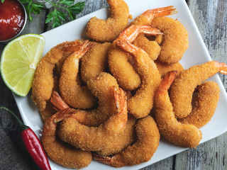 fried breaded shrimps served with lime and coriander leaves on white plate on wooden table, delicious deep, red, white sauce
