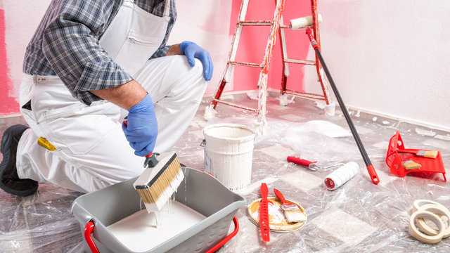 Caucasian house painter worker in white overalls, prepares the white paint to paint the pink wall. Construction industry. Work safety.