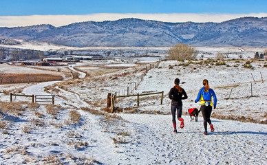 Joiggers with a dog run past a Colorado ranch in the snow
