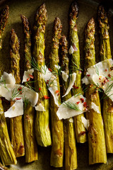 Grilled green asparagus sprinkled with parmesan cheese flakes, fresh dill and spices, top view, close up. Vegetarian food