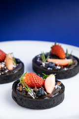 Cookie crust chocolate tart with Blueberry and strawberry set on Blue Background.
