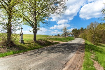 Fototapeta na wymiar Catholic cross at a country road in the Czech Republic. Easter Monday. Old asphalt road.