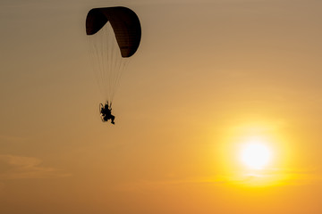 Silhouette of Paramotors flying to sky on sunset Adventure man active extreme sport pilot flying in sky with paramotor engine glider parachute. Paramotor flying on the sky at sunset. 