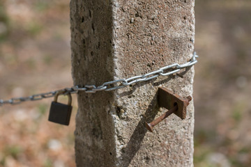 Close up of chain wrapped around a cement pole. In the background a rusty padlock, in the foreground a rusty screw.