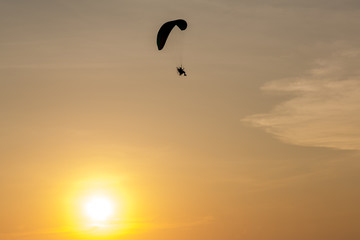 Silhouette of Paramotors flying to sky on sunset Adventure man active extreme sport pilot flying in sky with paramotor engine glider parachute. Paramotor flying on the sky at sunset. 