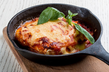 Lasagna in a cast iron pan on a wooden board. Traditional Italian dish