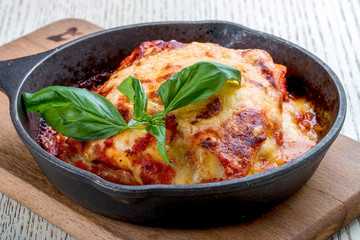 Lasagna in a cast iron pan on a wooden board. Traditional Italian dish