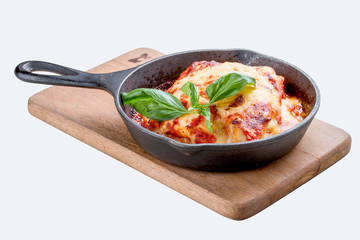 Lasagna in a cast iron pan on a wooden board. Traditional Italian dish