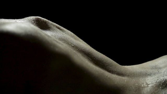 Sexy close-up of a woman's bare back as three marbles roll between her shoulder blades and down her back