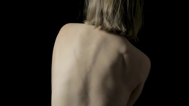 Close-up of a woman's naked back and shoulders as she sways side to side and rubs her shoulders and neck