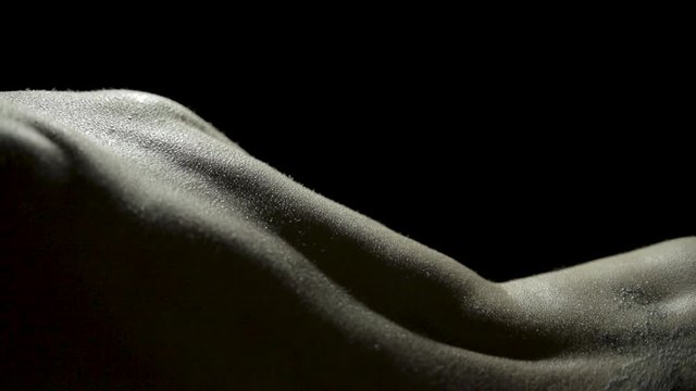 Sensual bodyscape of a woman's back glistening with sweat as she slowly turns, letting the dim light highlight her curves