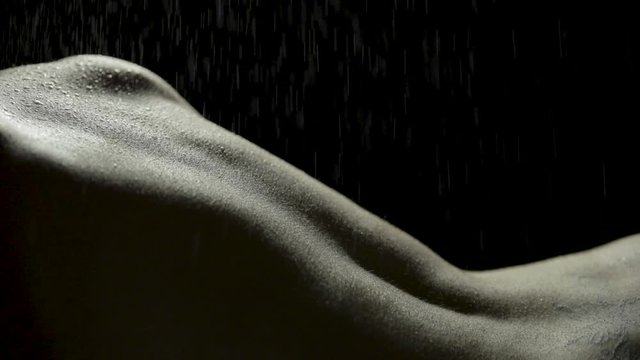 Close-up bodyscape of a woman's sexy back as she slowly turns with water misting down