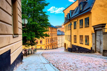 The narrow cobblestone street Bastugatan in Sodermalm with medieval houses in Stockholm at summer sunny day. - obrazy, fototapety, plakaty