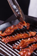 young woman in a gray apron fries bacon