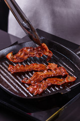 young woman in a gray apron fries bacon