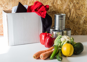 Donation concept empty box with clothes and food near the box on white table with wooden background 