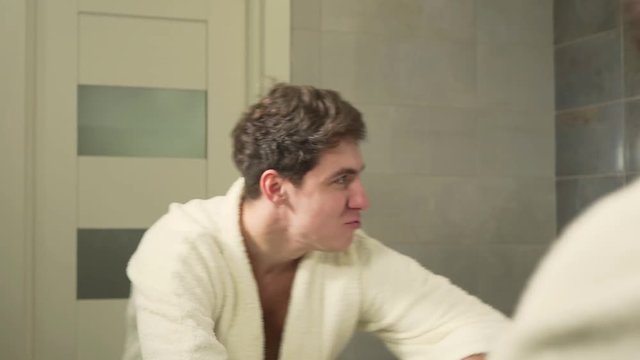 Young man is doing a funny movements while standing in front of a big mirror in a bathroom. Man is behaving himself like a big monkey - orang-outang.