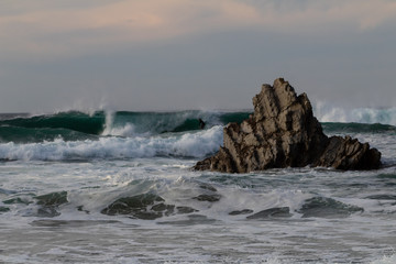 a surfer practicing surfing on Atxabiribil beach, next to a large rock, in the photo the sunset begins